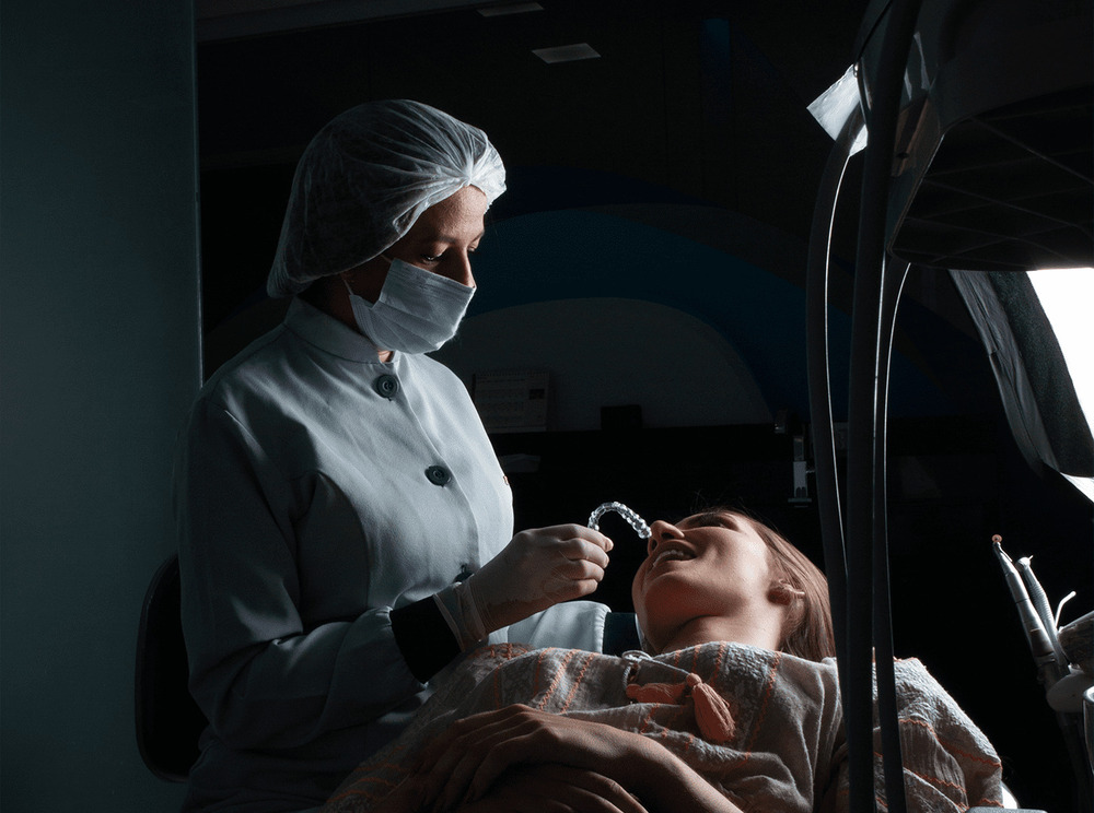 Imagem ilustrativa de uma dentista segurando o alinhador New Aligner próximo da boca de sua paciente